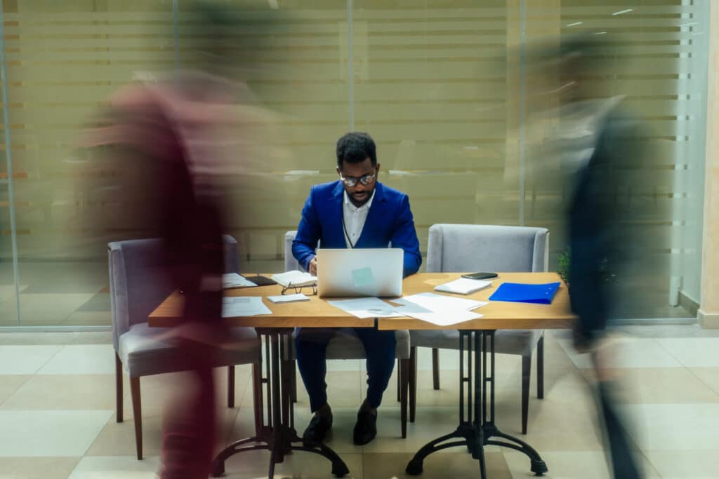 africa american business man working with laptop,blurred people walking next to him in big office.