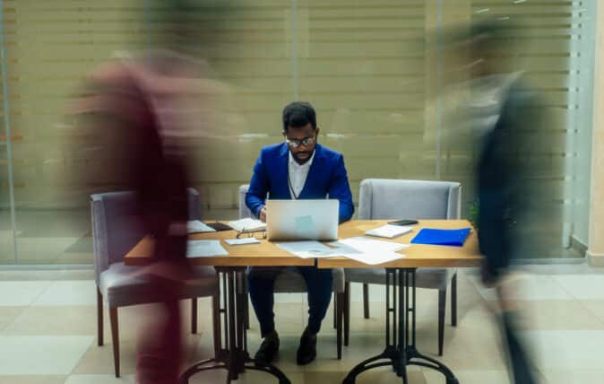 africa american business man working with laptop,blurred people walking next to him in big office.