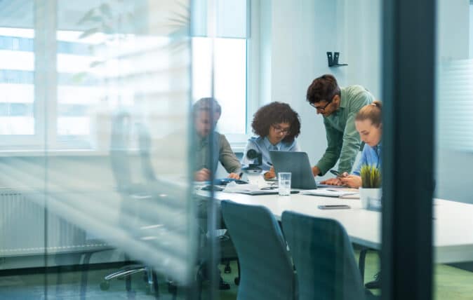 Office workers grouped around a laptop in a conference room