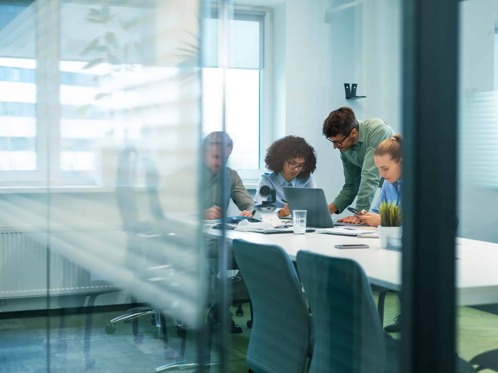 Office workers grouped around a laptop in a conference room