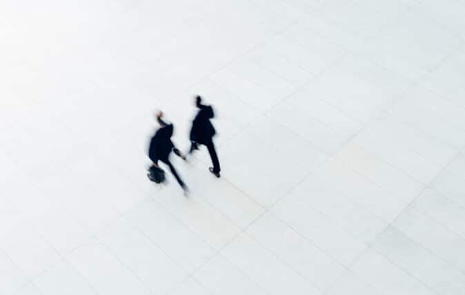 two men in suits and briefcases walk on white pavement