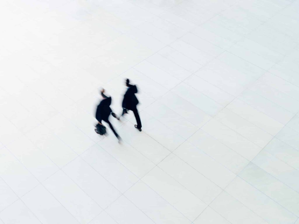 two men in suits and briefcases walk on white pavement