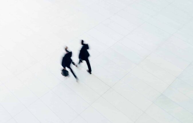 two men in suits and briefcases walk on white pavement